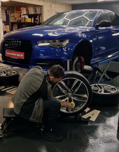 Aufbereiter reinigt die abgenommene Felge eines blauen Kombis in der Werkstatt